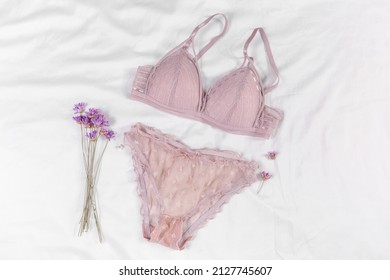 Sexy women's underwear and flowers on the bed. Pink color bra, lace lingerie on a white bedsheets background. Beauty blog concept. Top view, flat lay