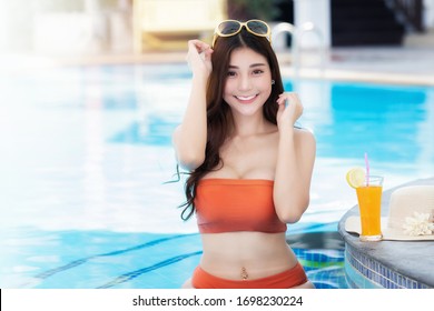 Sexy young asian woman in swimsuits in summer. beautiful woman in orange bikini with tropical drink sitting in swimming pool.