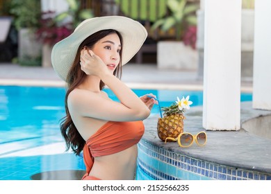 Sexy young asian woman in swimsuits in summer. beautiful woman in orange bikini with hat and tropical drink in swimming pool.