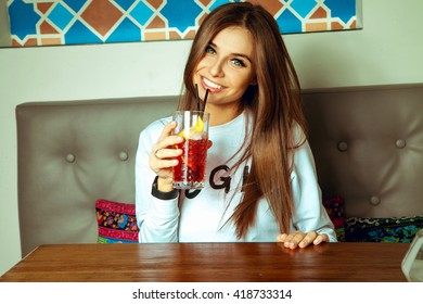 Sexy young brunette lady with green eyes drinks cocktail and smiling on camera