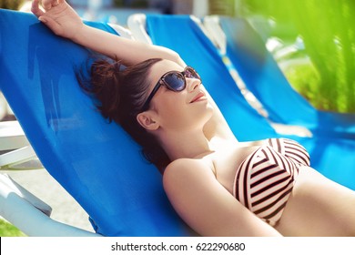 Sexy young brunette taking sunbath at swimming pool