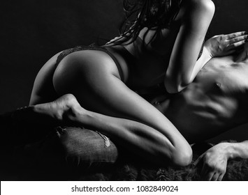 Sexy young couple of undressed sensual woman with straight body in red lace erotic lingerie sitting above muscular man kissing posing indoor on dark background, horizontal picture