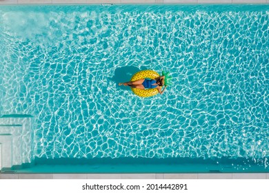 Sexy Young Female In Swimsuit Bikini, In A Straw Hat And Sunglasses Floating On Blue Swimming Pool Waves On Giant Inflatable Yellow Pineapple Tube. Chill Out Summer Vacation In Luxury Resorts Concept.