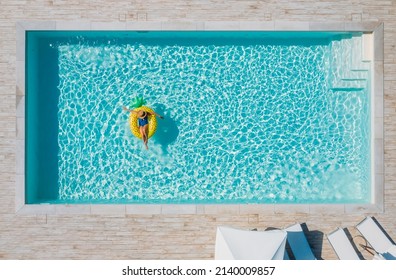 Sexy Young Female In Swimsuit Bikini, In A Straw Hat And Sunglasses Floating On Blue Swimming Pool Waves On Giant Inflatable Yellow Pineapple Tube. Chill Out Summer Vacation In Luxury Resorts Concept.