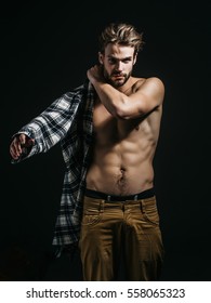 Sexy young handsome naked man with messy hair, in beige pants wears plaid shirt on dark background