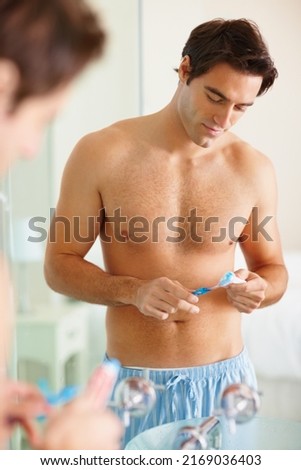 Sexy young man applying paste to his toothbrush. Handsome shirtless guy applying toothpaste to his brush in front of the mirror.