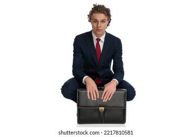 Sexy Young Man In Elegant Suit With Long Hair Crouching Next To Suitcase And Posing In Front Of White Background