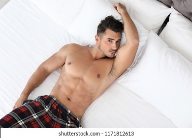 Sexy Young Man Lying On Bed With Soft Pillows At Home, Top View