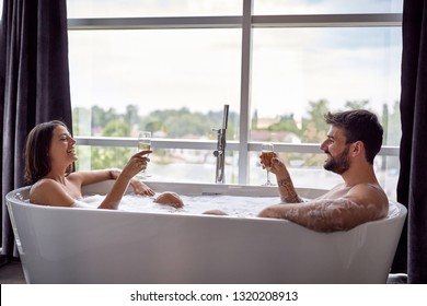 Sexy young man and woman have fun together in the bathtub and drinking champagne