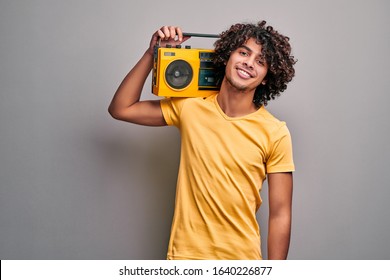 Sexy young man in yellow t-shirt and yellow beatbox on shoulder on isolated gray background. Arabian student listenig retro music on vintage player