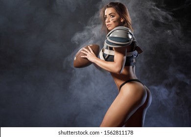 Sexy young quarterback girl with ball in smoke. American football