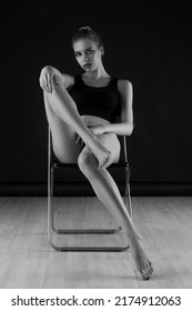 Sexy young woman with long legs sitting on chair, studio portrait. Monochrome