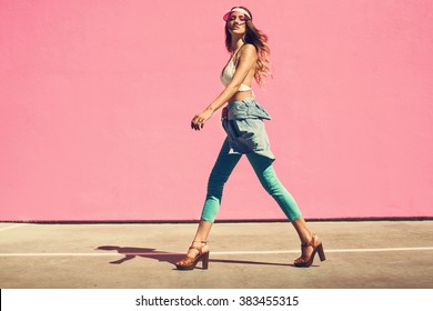Sexy young woman walking in a city next to pink wall in jeans shirt and mint pants. Fashion summer photo