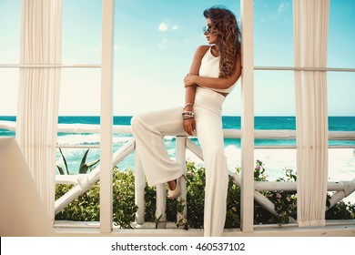 Sexy Young Woman In White Clothes Posing In The Garden By The Sea. Fashion Summer Photo. Bright Colors, Sunglasses