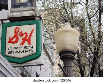 An S&H Green Stamp sign. with a lamp post in the foreground.