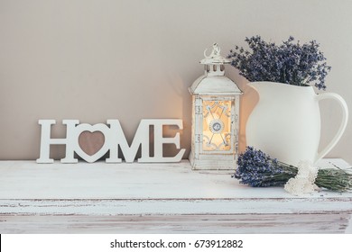 Shabby chic interior decor for farmhouse. Lavender in pitcher, lantern and wooden letters on a vintage shelf over pastel wall. Provence home decoration.