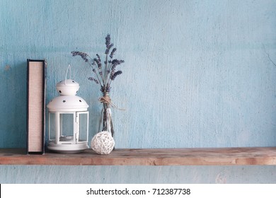 Shabby old interior decor for farmhouse. Lavender in glass vase and book,candle on a vintage shelf over pastel wall. Home decoration.