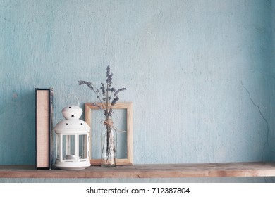 Shabby old interior decor for farmhouse. Lavender in glass vase and blank photo frame,book,candle on a vintage shelf over pastel wall. Home decoration.