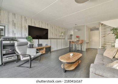 Shabby Wooden Table With Chairs And Vase Located Near Comfortable Couch Against Light Walls With Decorations And TV In Modern Apartment