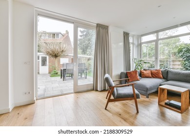 Shabby Wooden Table With Chairs And Vase Located Near Comfortable Couch Against Light Walls With Decorations And TV In Modern Apartment