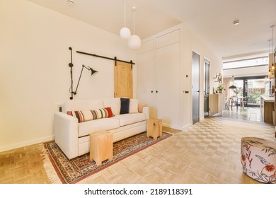 Shabby Wooden Table With Chairs And Vase Located Near Comfortable Couch Against Light Walls With Decorations And TV In Modern Apartment