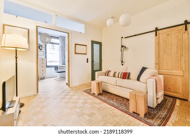 Shabby Wooden Table With Chairs And Vase Located Near Comfortable Couch Against Light Walls With Decorations And TV In Modern Apartment