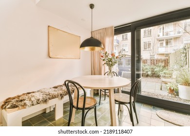 Shabby Wooden Table With Chairs And Vase Located Near Comfortable Couch Against Light Walls With Decorations And TV In Modern Apartment