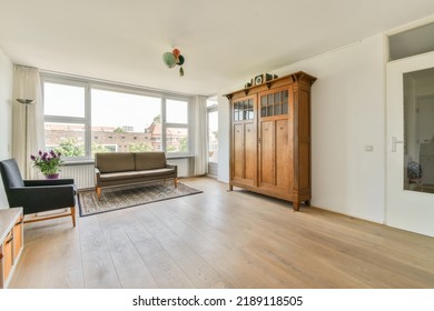 Shabby Wooden Table With Chairs And Vase Located Near Comfortable Couch Against Light Walls With Decorations And TV In Modern Apartment