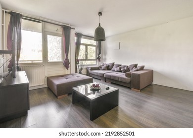 Shabby Wooden Table With Chairs And Vase Located Near Comfortable Couch Against Light Walls With Decorations And TV In Modern Apartment