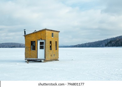 Shack made of plywood for ice fishing on a frozen lake with trees in the background
