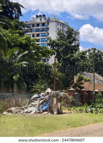 a shack on a city street against the background of a high-rise expensive residential building. The homeless man's home. Differentiation of income of the population. Poverty and wealth concept.