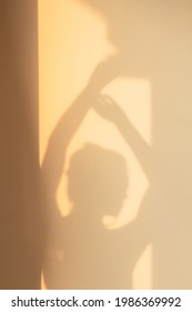 Shade silhouette of young woman with hair bun on wall at home in evening sunlight. Window shadow of girl dancing with hand up. Concept of rest, home, joy, lifestyle, aesthetics, freedom, background.
