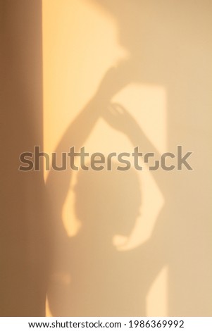 Shade silhouette of young woman with hair bun on wall at home in evening sunlight. Window shadow of girl dancing with hand up. Concept of rest, home, joy, lifestyle, aesthetics, freedom, background.