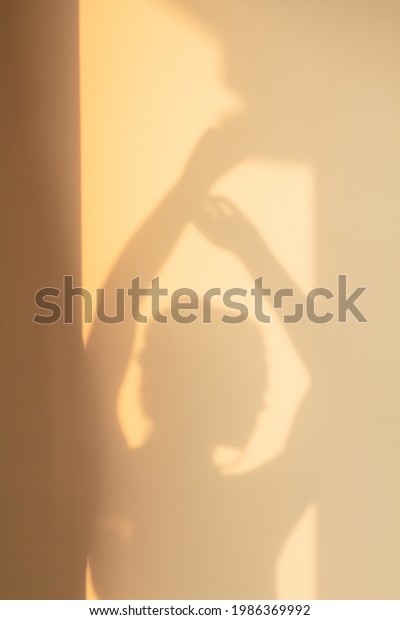 Shade silhouette of young woman with hair bun\
on wall at home in evening sunlight. Window shadow of girl dancing\
with hand up. Concept of rest, home, joy, lifestyle, aesthetics,\
freedom, background.