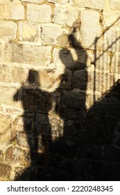 Shadow Of 2 People On The Wall. People Standing On A Staircase And One Waving. Sunlight. Old Stone Wall.