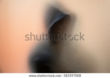 Shadow blur of horror man in jacket with hood.Dangerous man behind the frosted glass.Mystery man.Halloween background.Blur picture