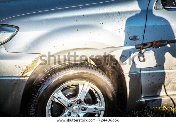 A shadow of a boy with a high
pressure washer on a grey dirty car in a sunny summer
day

