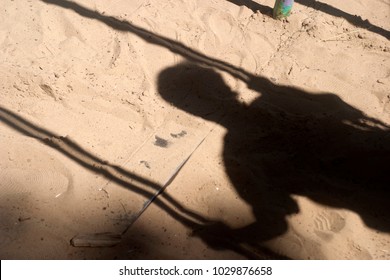 Shadow of a boy in the sand, which is riding on a swing in the playground. Summer and autumn background