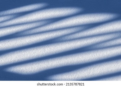 The shadow of a cast-iron fence in the snow on a sunny winter day