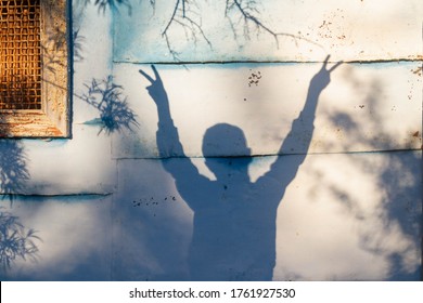 The Shadow Of A Child On The Fence, The Boy Raised His Hands In Victory. Finger Sign, Two Fingers Up.