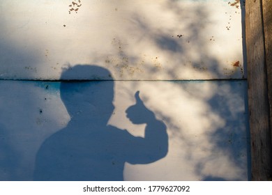 Shadow of a child on the fence, boy like, thumbs up. Blue background. Teenager.