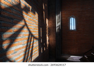 Shadow of clock tower casts intriguing pattern on brick wall inside building with small arched window. Clock tower
