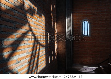 Shadow of clock tower casts intriguing pattern on brick wall inside building with small arched window. Clock tower
