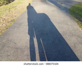 Shadow In Driveway Of Man Taking Out The Garbage Can