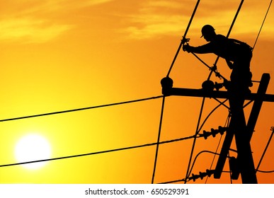 Shadow electricians repairing wire on electric power pole at the sunsetbackground blur.