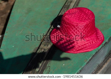A shadow of a hand touching pink bucket hat lying on the green surface.