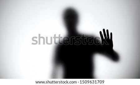 Shadow of man holding glass wall, trying to escape from captivity, kidnapping