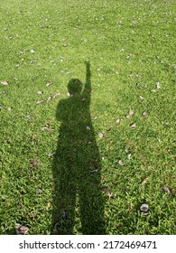 Shadow Of A Man Holding Up Two Fingers Standing On A Green Grass In The Morning.