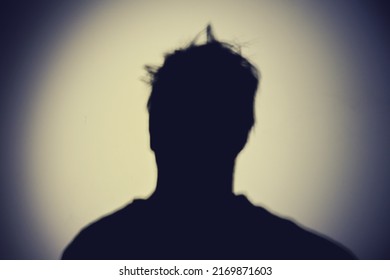 Shadow Of A Man From The Night Light Of A Flashlight On A White Wall. Silhouette Of A Man Head From The Light Of A Lamp