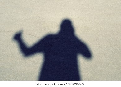 Shadow of a man on the pavement with a camera in his hands and shows a thumb up. Top view of the front.